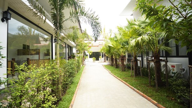 A pathway flanked by lush greenery and modern buildings, leading to a central entrance. - iRest Ao Nang Seafront (Krabi)