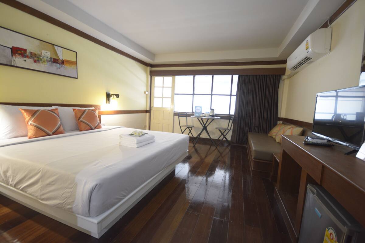 A hotel room with a large bed, a desk, a television, and an air conditioning unit.