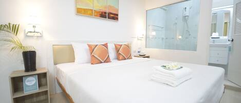 Una habitación de hotel con una cama grande, una mesita de noche con lámpara, una planta en maceta y un cuadro en la pared.