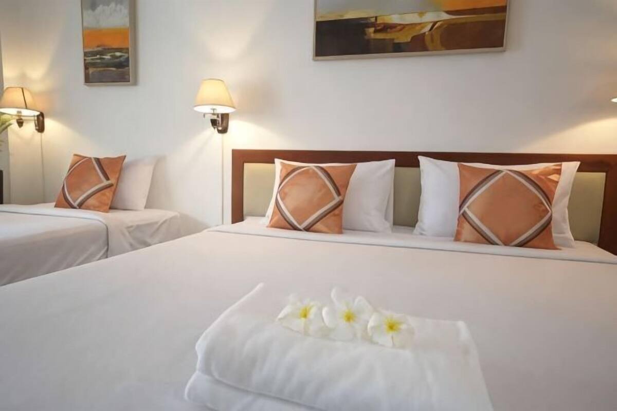 A hotel room with two beds, each with matching headboards and pillows, and a neatly made bed with a white towel and flowers.