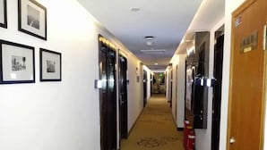 A hotel hallway with framed pictures on the walls, doors on the sides, and a carpet with a floral pattern. - Cotton hotel (Chengdu)