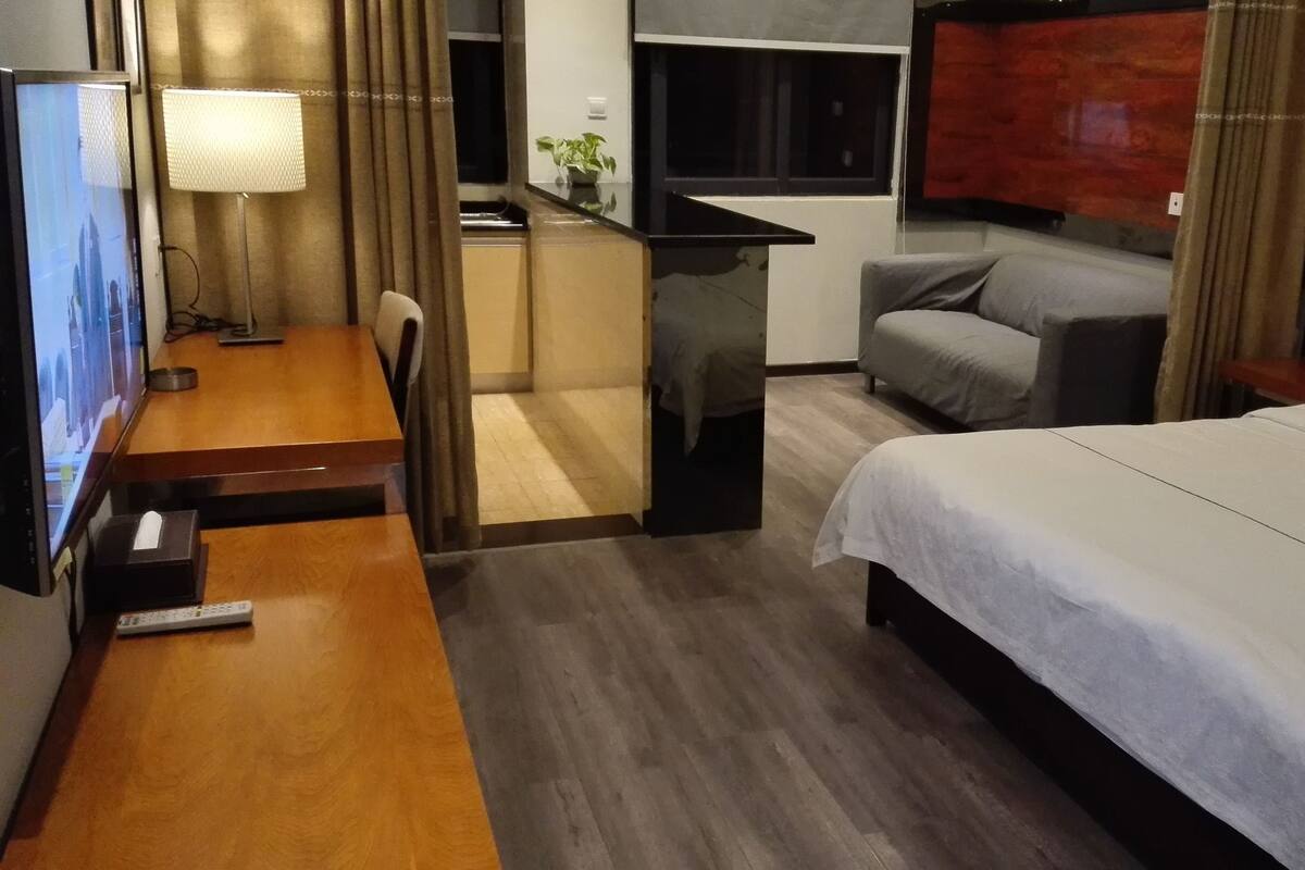 Habitación de hotel con cama, escritorio con lámpara, televisión y un pequeño rincón con kitchenette.