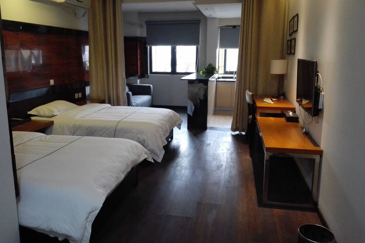 Una habitación de hotel con dos camas, un escritorio, una silla, un televisor y una ventana pequeña.