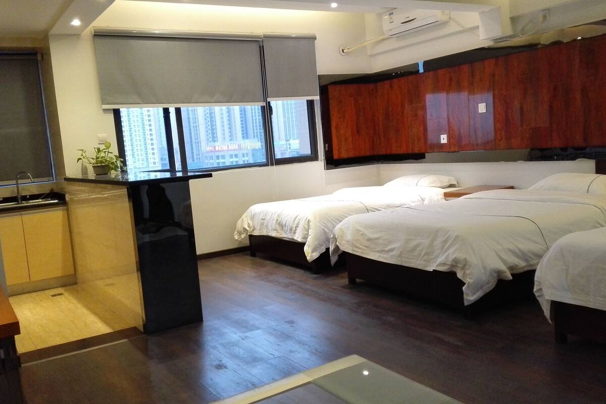 Habitación de hotel con dos camas, una kitchenette pequeña, una ventana con vistas a edificios y piso de madera.