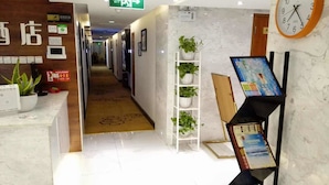 A hotel reception area with a marble floor, a reception desk, a clock, and a plant shelf. - Cotton hotel (Chengdu)