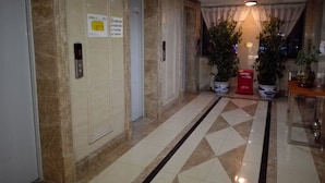 A hotel lobby with marble flooring, a reception desk, potted plants, and elevator doors. - Cotton hotel (Chengdu)