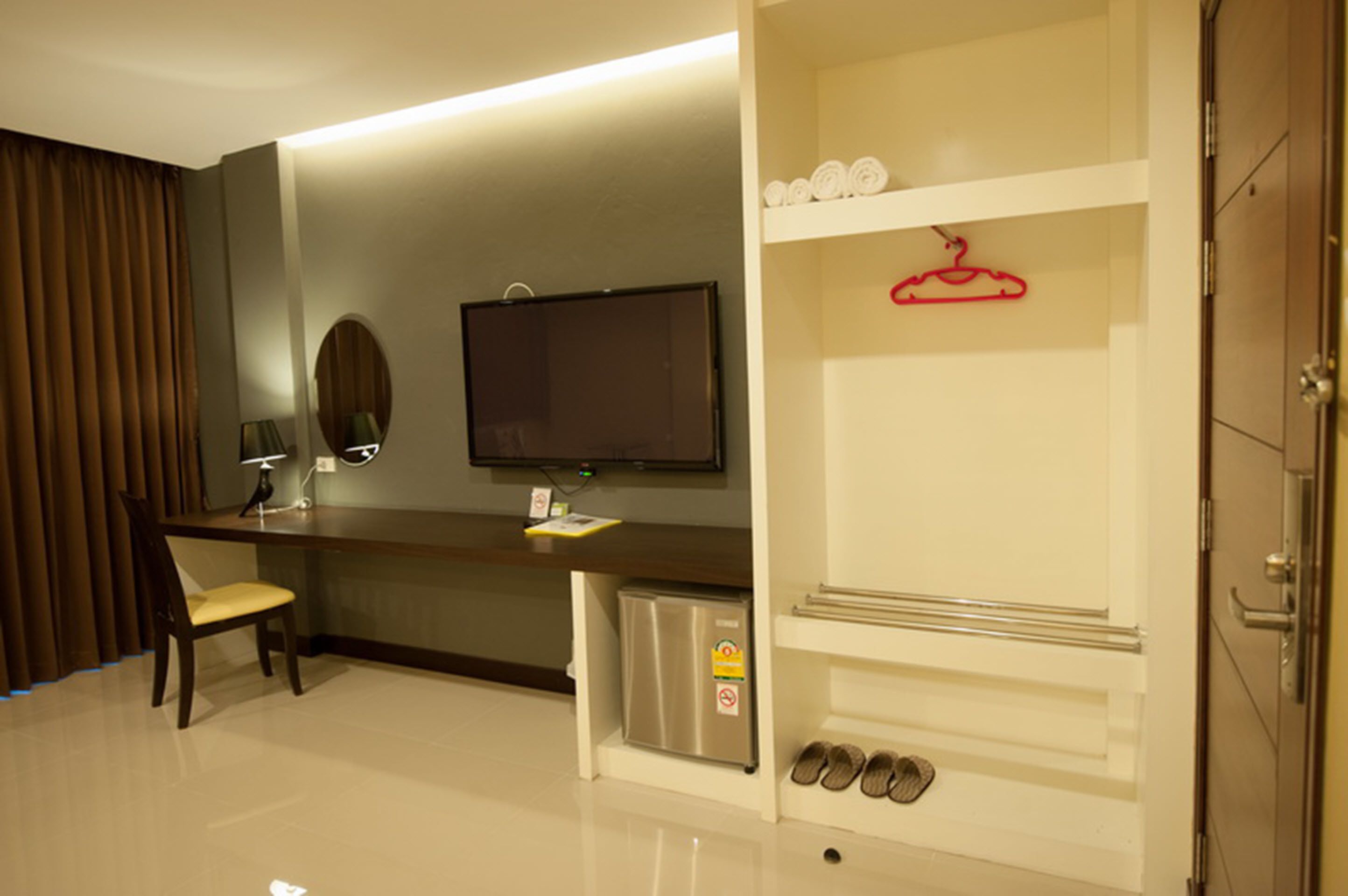 Une chambre d’hôtel équipée d’un bureau, d’une chaise, d’une télévision, d’un minibar et d’un porte-chaussures.