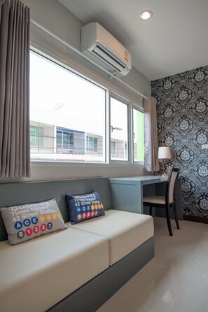 A room with a bed, a desk, and a chair. There is a window with curtains, an air conditioner, and a lamp on the desk. - The Cozy Nest Boutique Rooms (Phayao)
