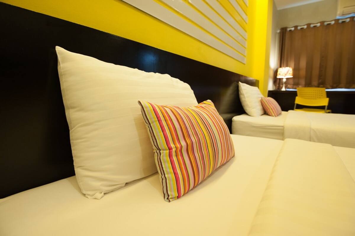 A hotel room with two beds, each with white bedding and striped pillows. The room features a black headboard and a yellow accent wall.