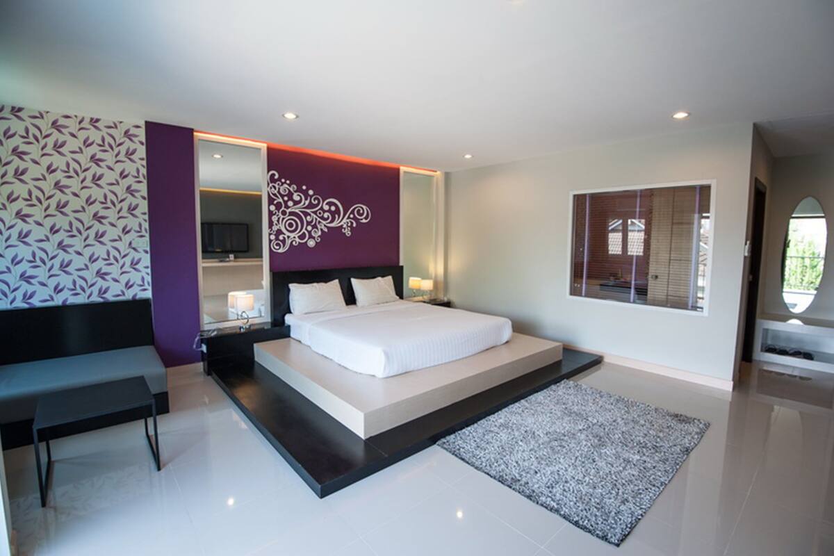 A modern bedroom with a large bed, a bench, a TV, and a decorative wall.