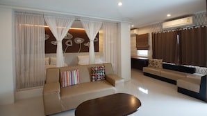 A modern living room with a beige sofa, a coffee table, and a TV. There are curtains and an air conditioning unit on the wall.