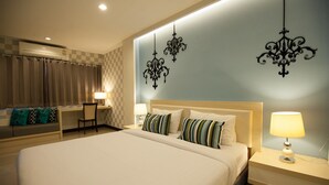 A hotel room with a large bed, a desk with a chair, a nightstand with a lamp, and decorative wall sconces.