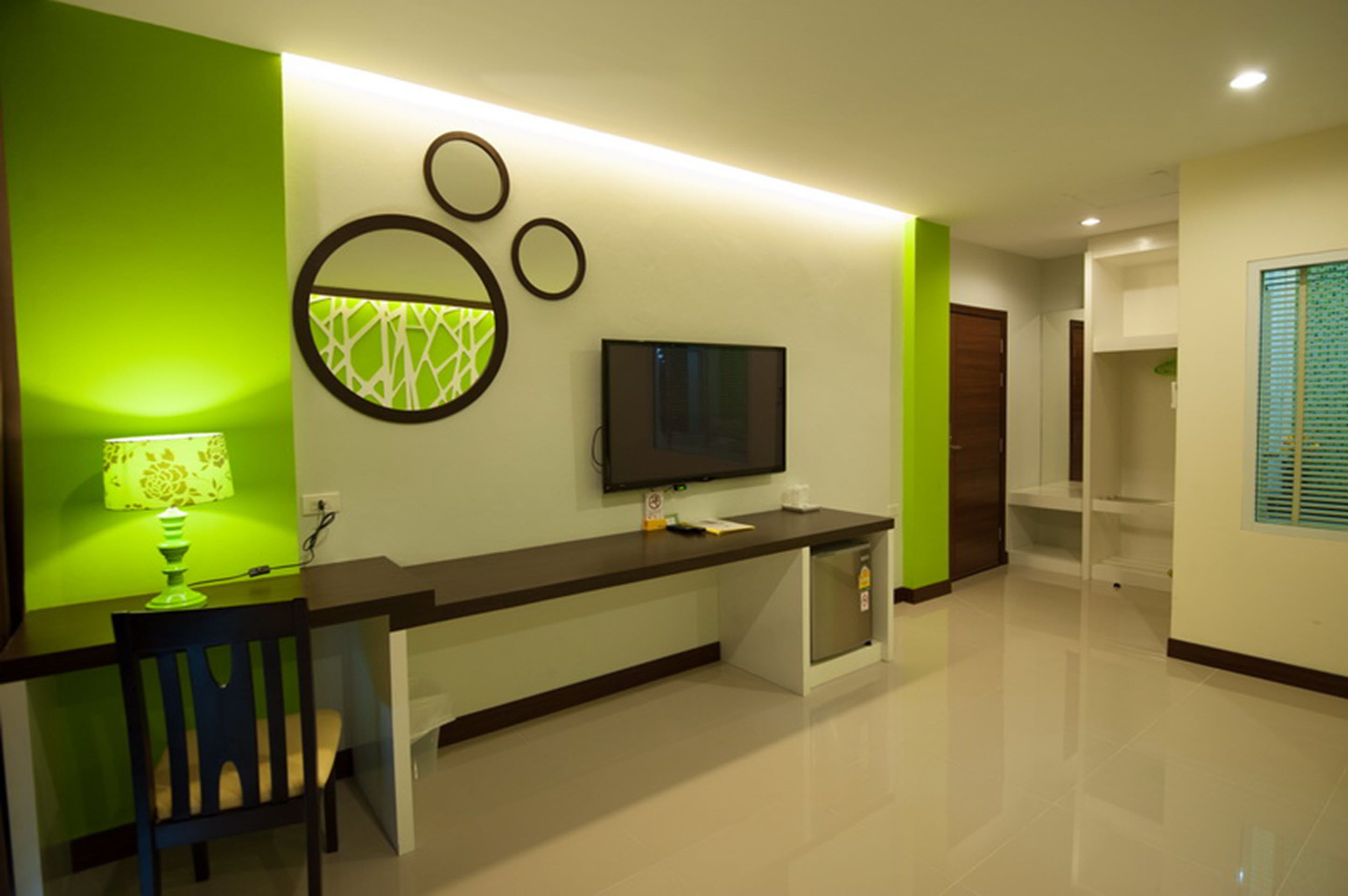 Een moderne hotel receptie met een groene accentmuur, een flatscreen televisie boven een balie en een fauteuil met een lamp.