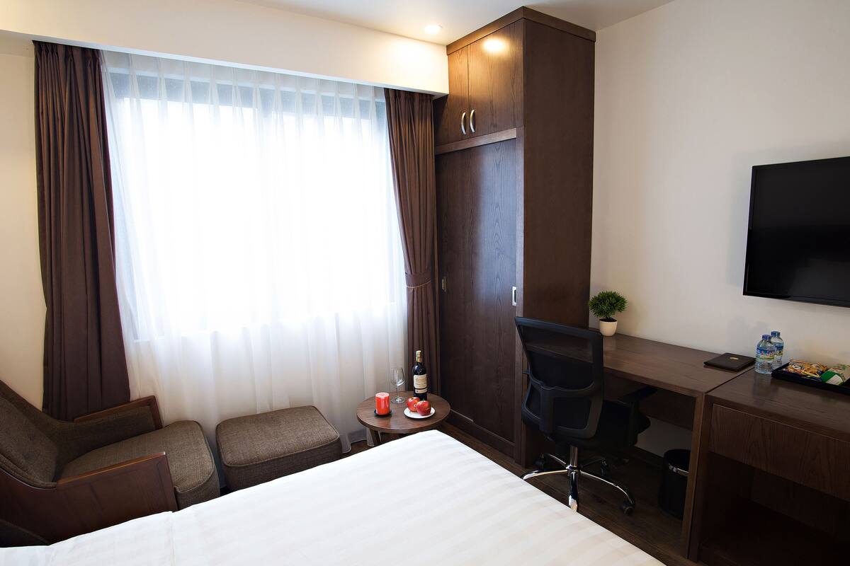 Habitación de hotel con cama, dos sillones, un escritorio con silla, televisión y ventana con cortinas.