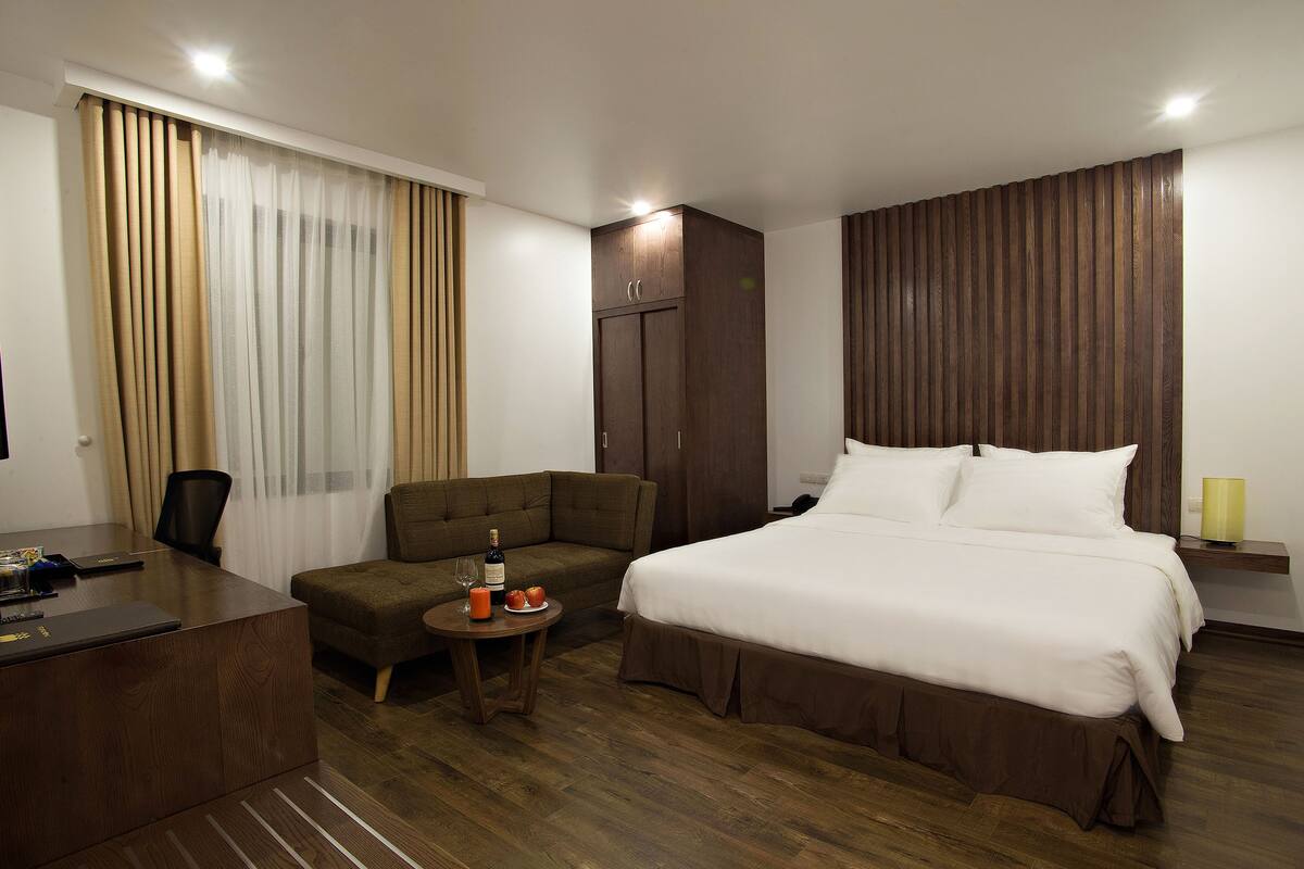 Habitación de hotel con cama, escritorio, silla, una mesita con una botella y vasos, y un armario.
