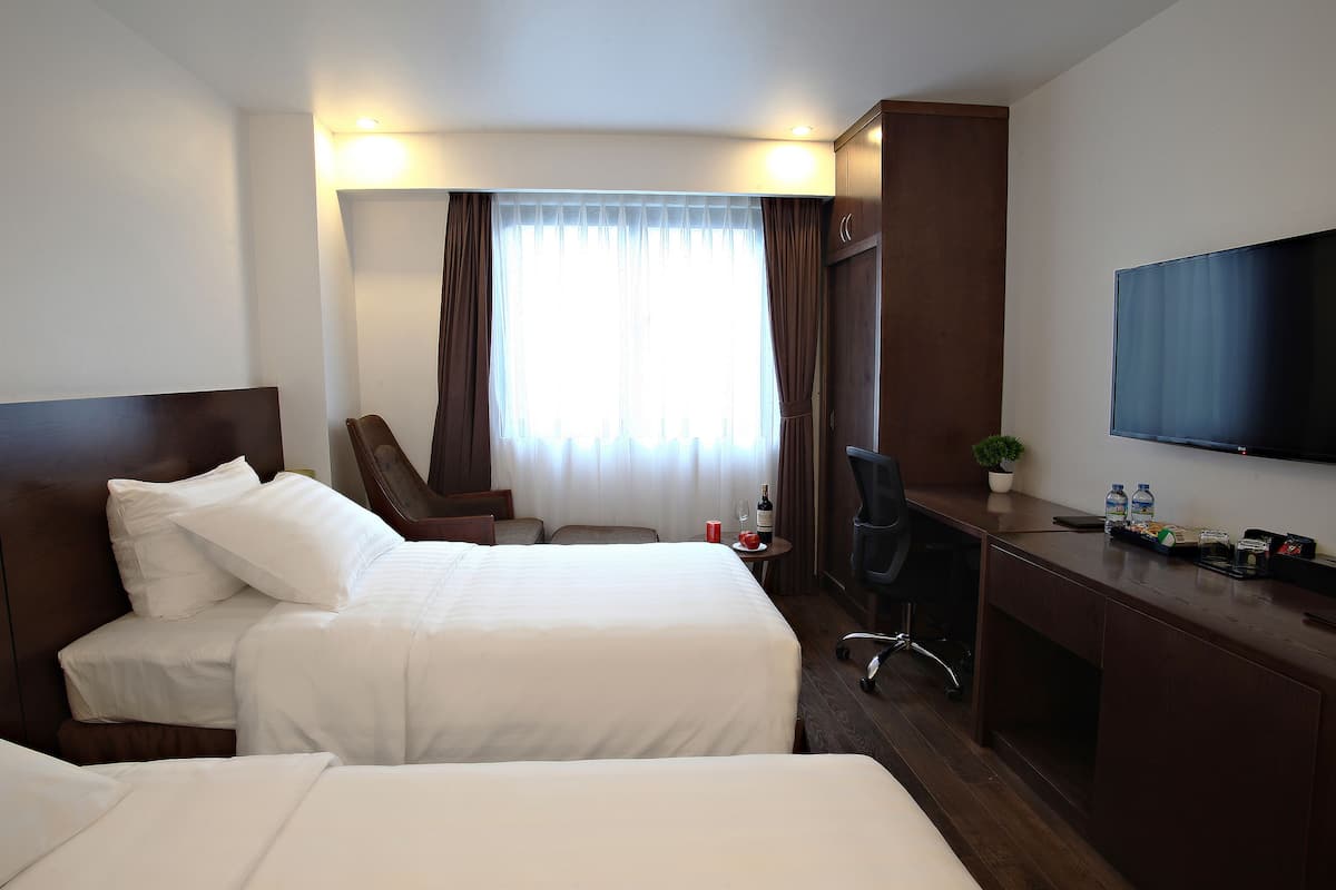 Una habitación de hotel con dos camas, un escritorio con silla, un televisor y una ventana con cortinas.