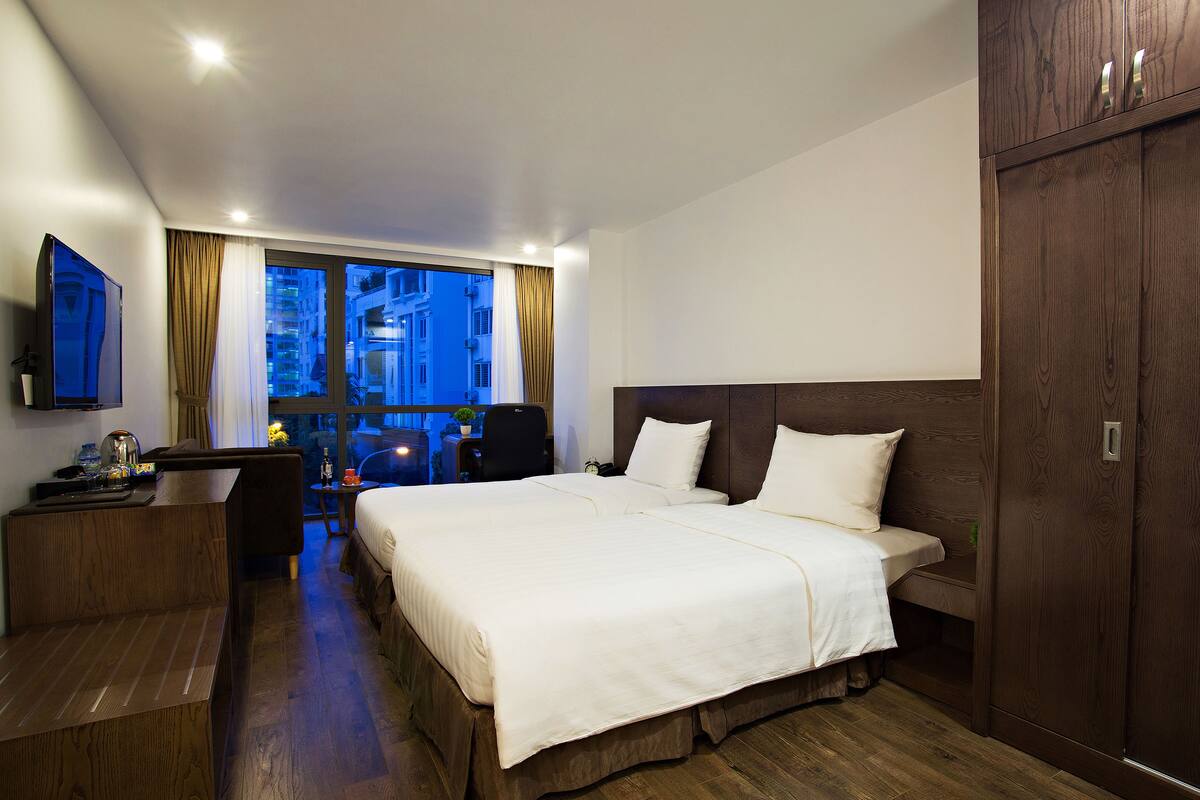 Habitación de hotel con una cama grande, un escritorio, un televisor y vistas a la ciudad a través de la ventana.