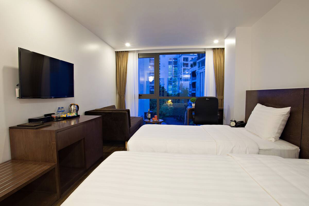 Habitación de hotel con cama, escritorio con televisor, una silla y vista nocturna de la ciudad.