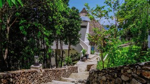 Una scala in pietra conduce a un edificio con tetto di paglia, immerso nel verde.