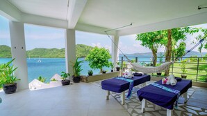 Un'area benessere con due lettini da massaggio, un'amaca e vista su un lago con barche a vela.