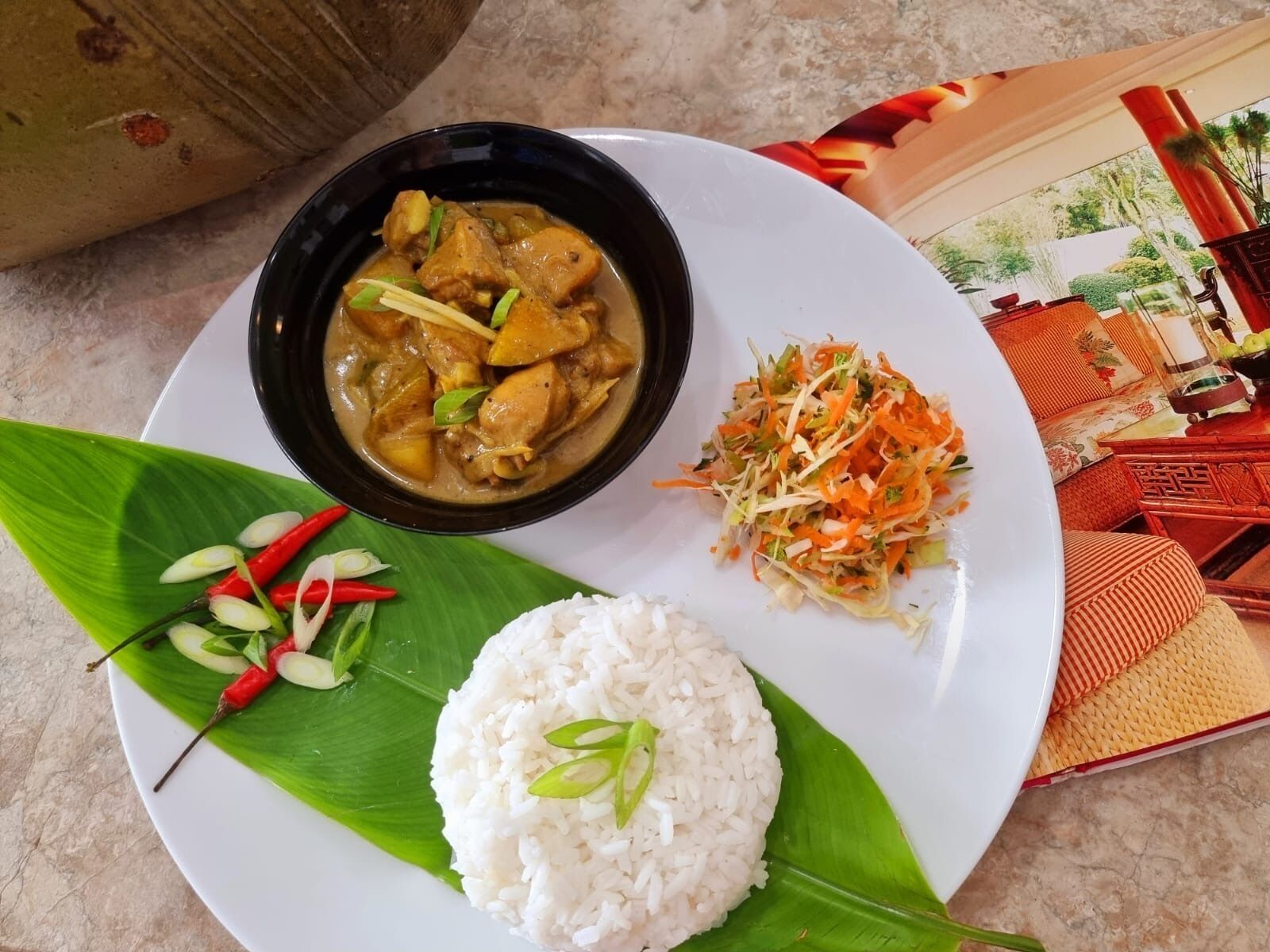 A plate with white rice, a bowl of curry, and a side salad, served on a banana leaf.
