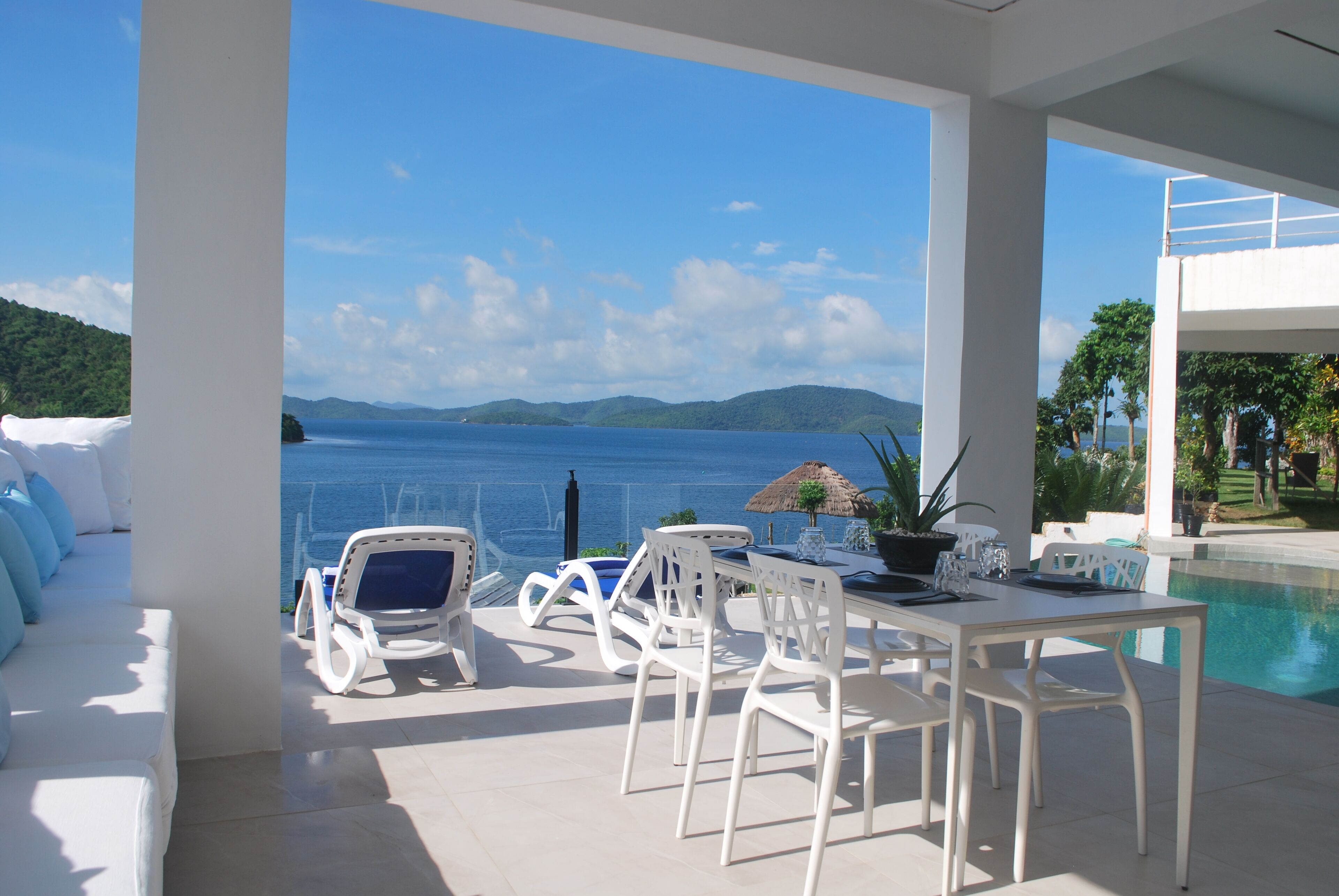 A modern outdoor seating area with a pool, white furniture, and a view of the sea.
