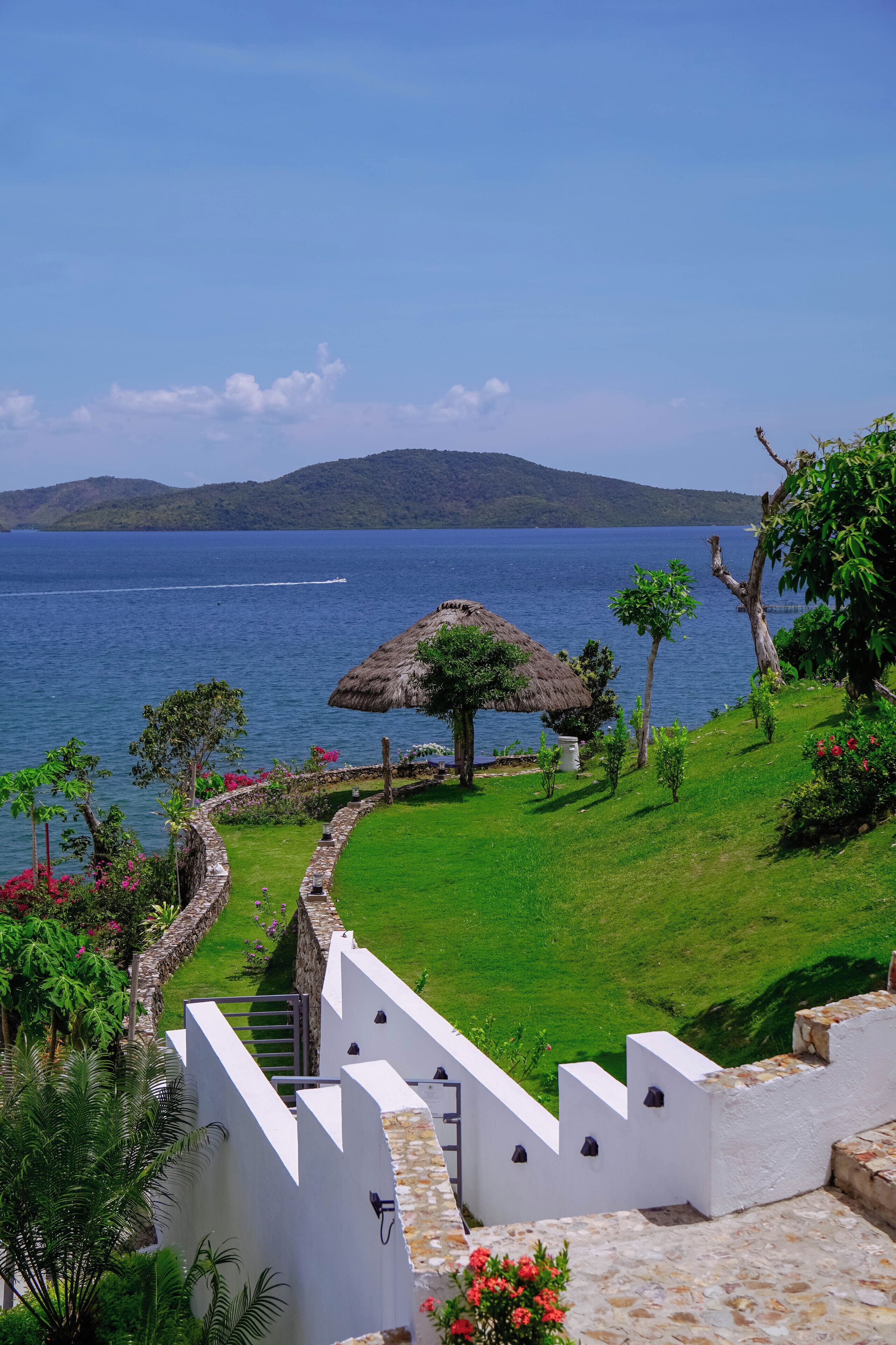 A coastal view with a thatched-roof structure, a stone staircase, and a lush green landscape.