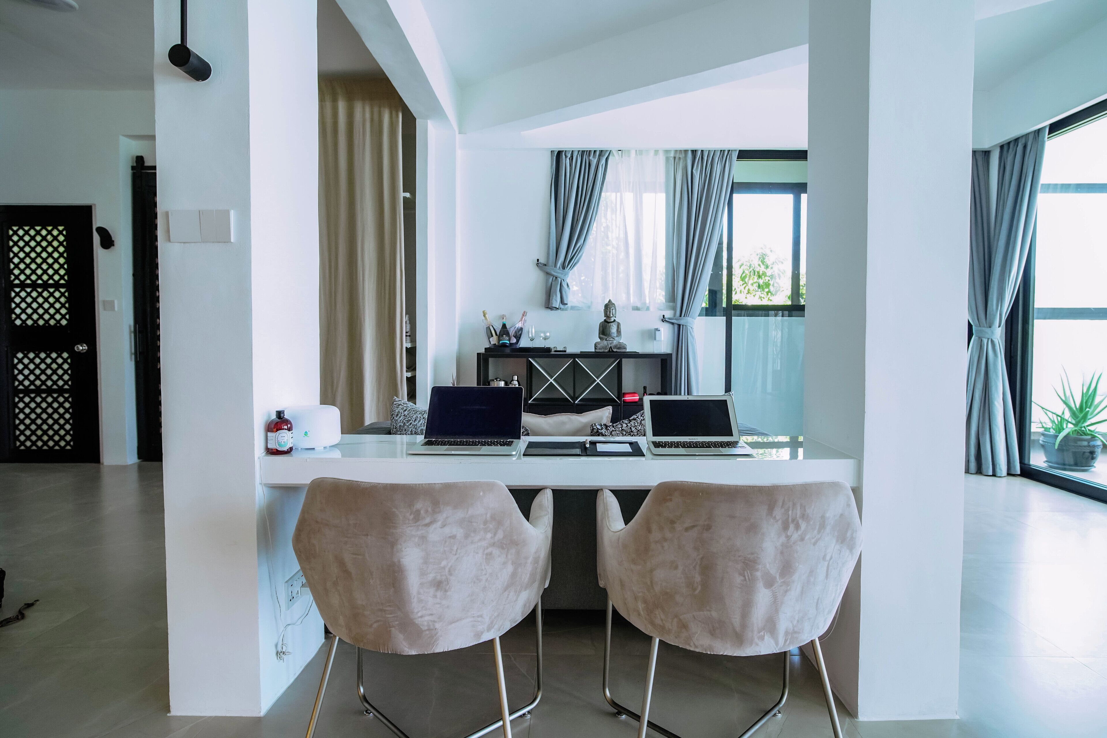 Una cocina moderna con dos portátiles sobre una isla blanca, una estatua de Buda y una ventana con cortinas.
