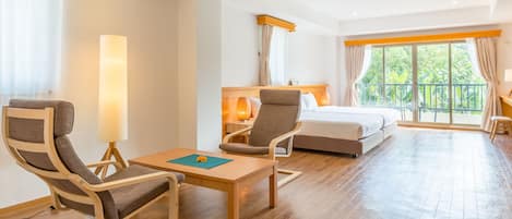 A hotel room with a bed, two armchairs, a table, and a large window with curtains.