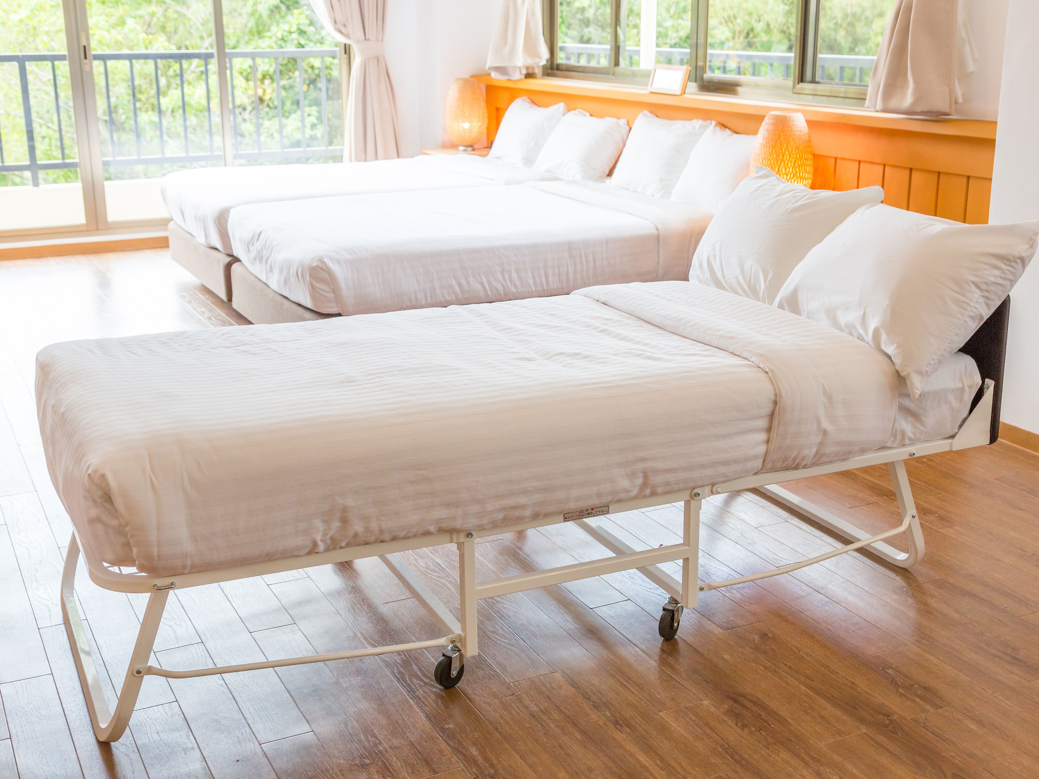 Habitación de hotel con dos camas, suelo de madera y ventana con cortinas.