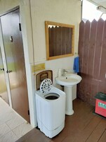 Un baño pequeño con lavadora, lavamanos y puerta de madera.