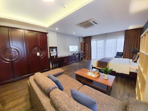 A hotel room with a sofa, a bed, a desk with a computer, a TV, and a large window. - Cherry Hotel 1 (Hanoi)