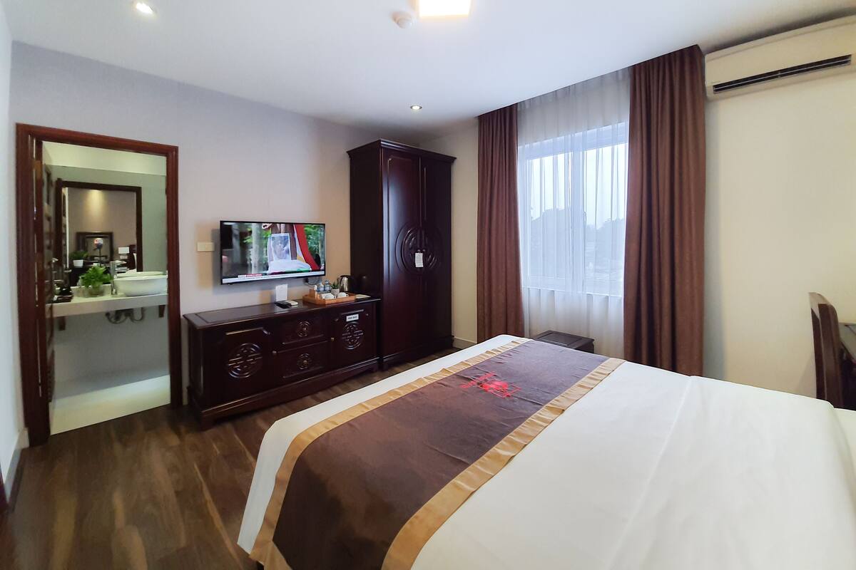 Una habitación de hotel con cama, televisión, cómoda, espejo y ventana con cortinas.