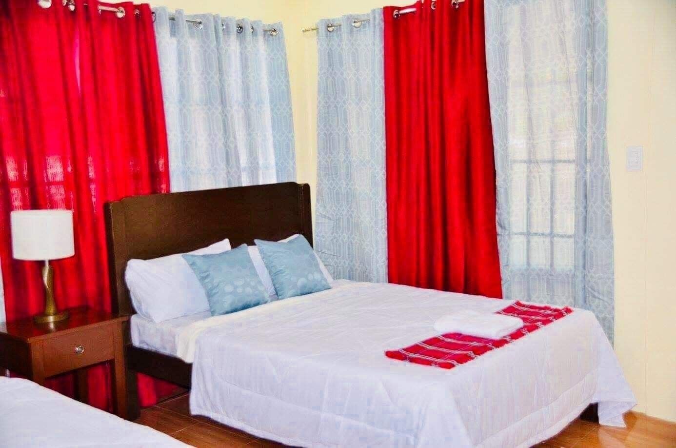 A hotel room with a bed, a nightstand, a lamp, and red and white curtains.