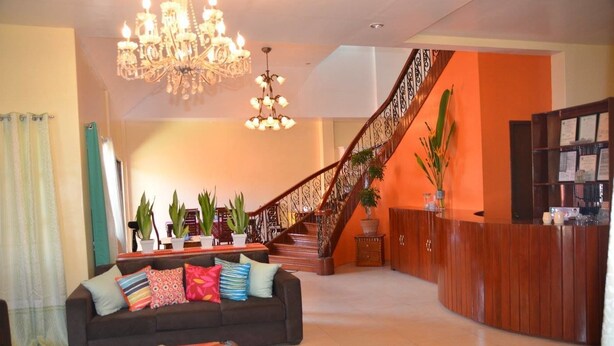 A spacious lobby with a dark brown sofa, colorful cushions, a chandelier, a staircase, and a reception desk. - Umaverde Bed & Breakfast (San Jose de Buenavista)