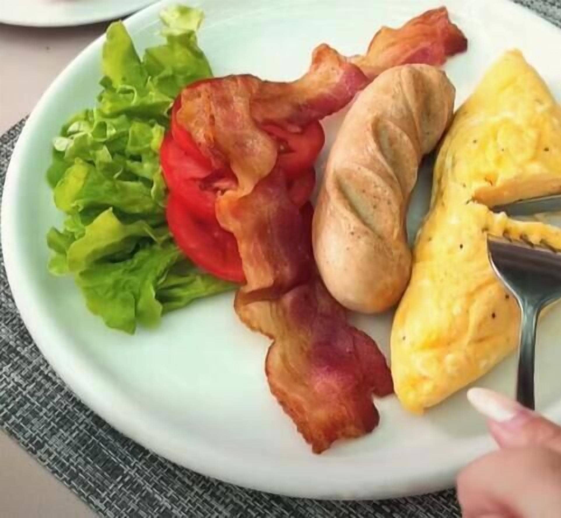 Un plato con tocino, huevos revueltos, una rodaja de tomate y lechuga.