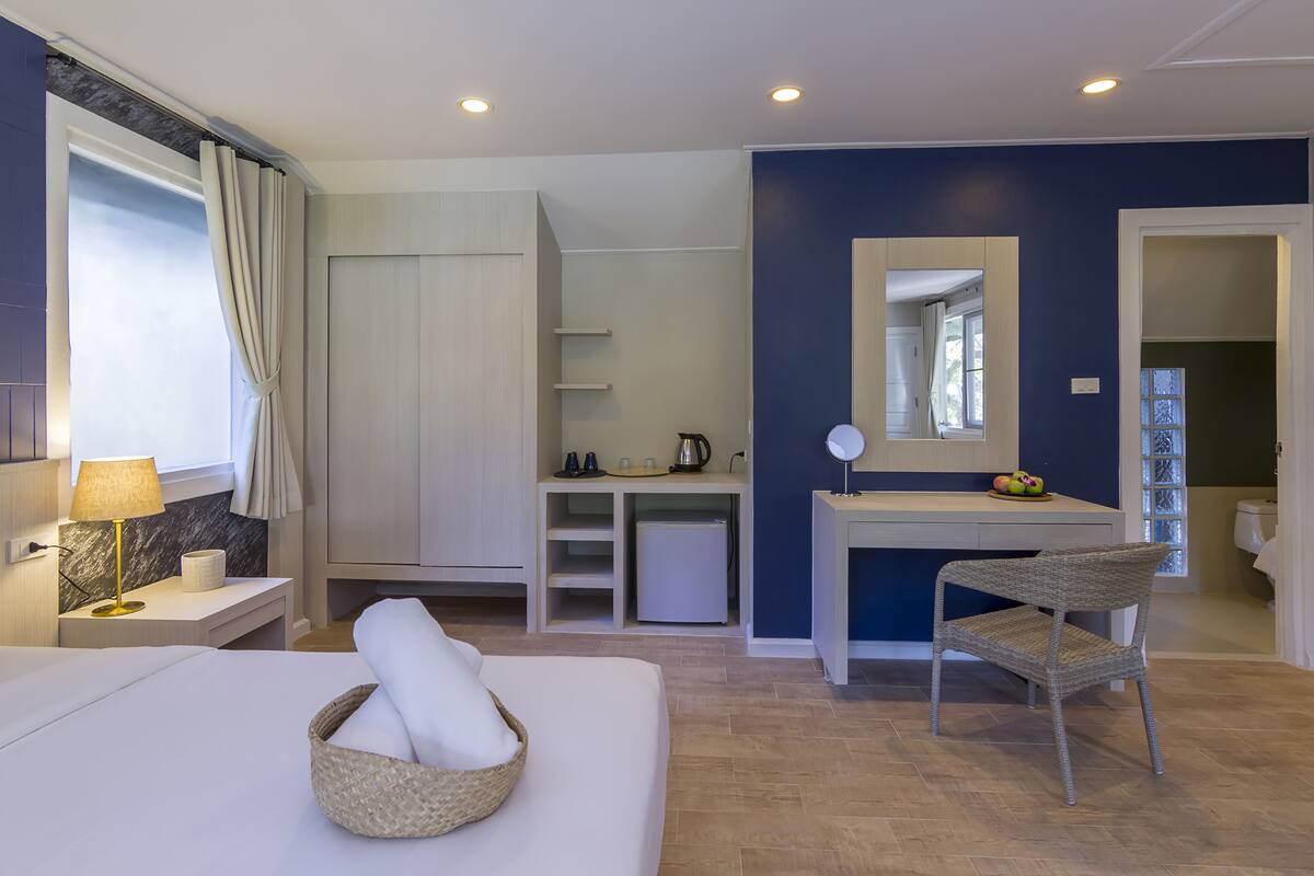 Una habitación de hotel moderna con una cama, un escritorio, una silla, un refrigerador pequeño, un espejo y una ventana con cortinas.