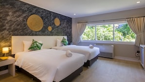 Une chambre d’hôtel avec deux lits, une grande fenêtre avec des rideaux, un mur décoré de motifs circulaires et une lampe de chevet.