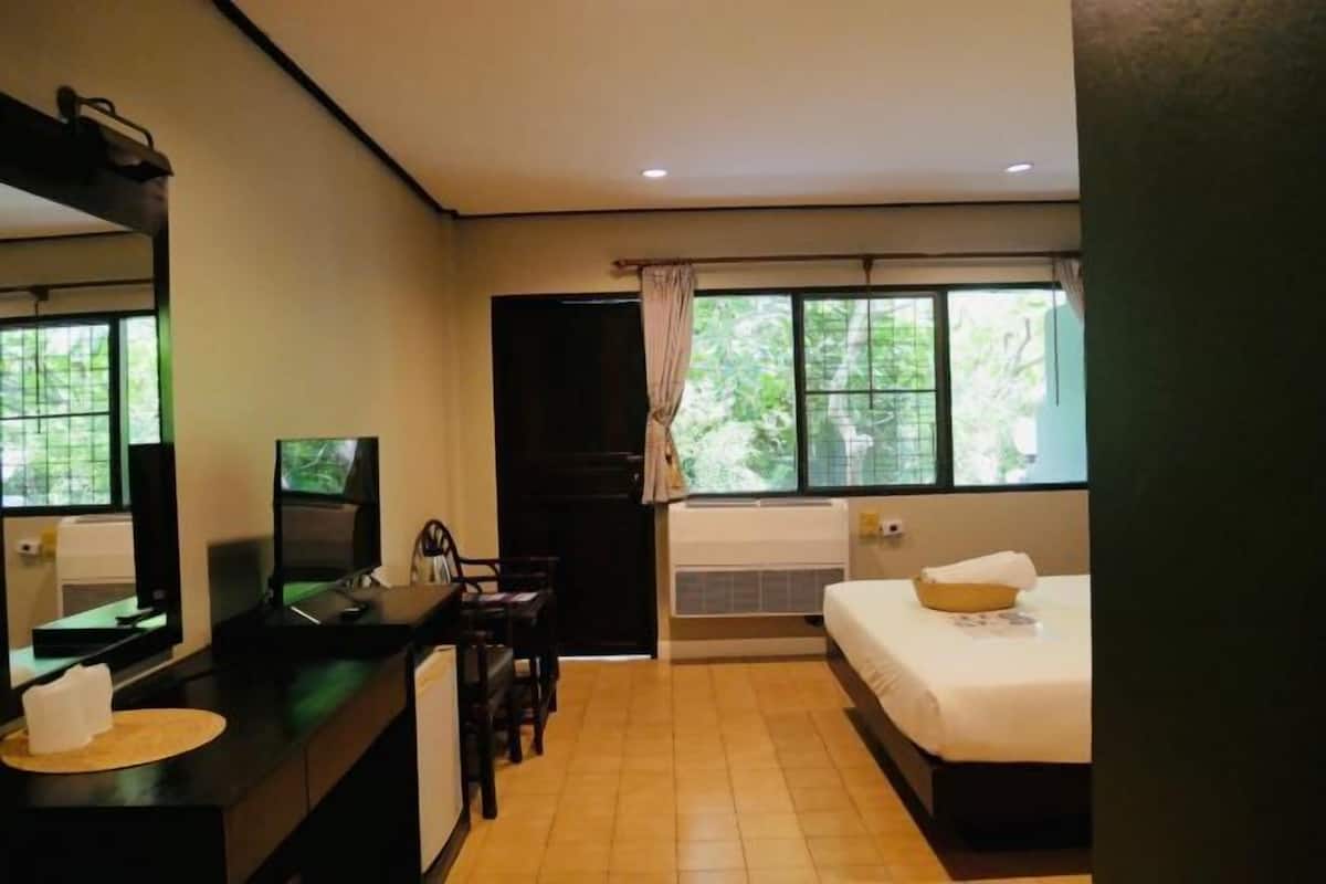 Una habitación de hotel con cama, escritorio, silla, televisión y ventana con cortinas.