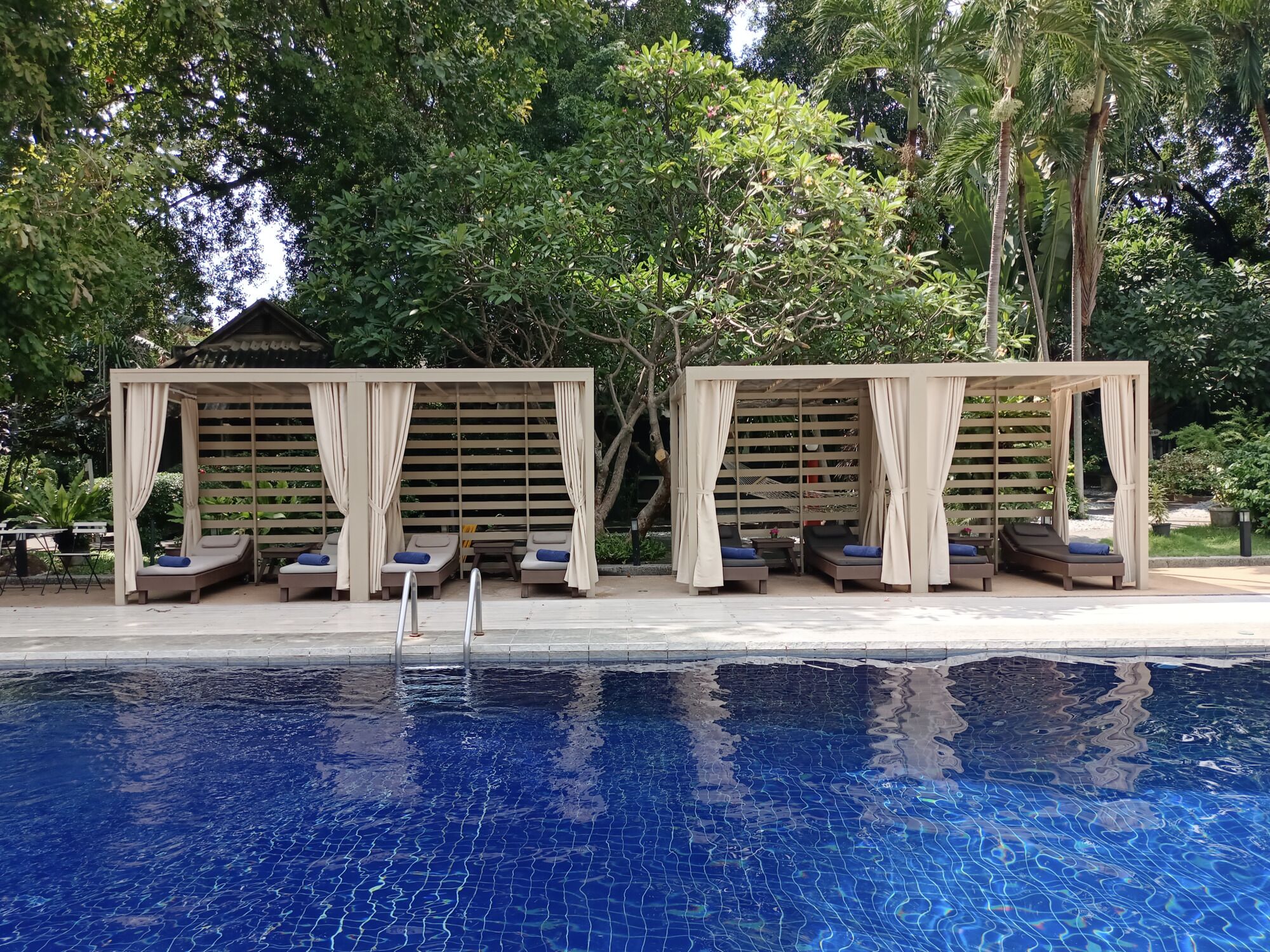 Un área de piscina con dos gazebos de madera, cada uno con asientos acolchados y cortinas.