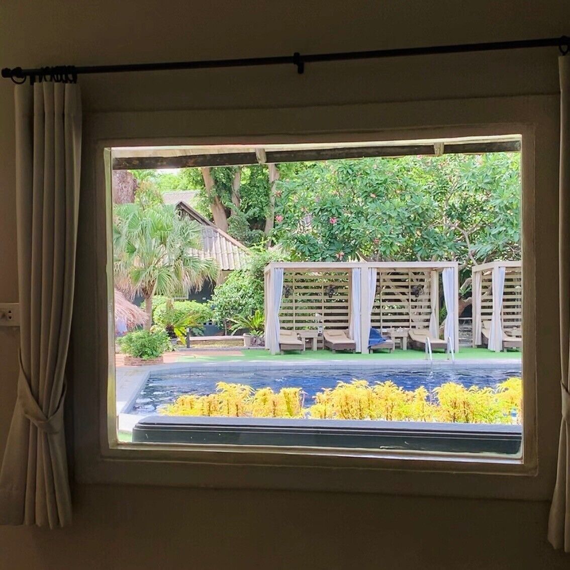Ein Fenster mit Blick auf einen Garten, eine Holz-Pergola und ein Schwimmbad.