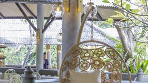Un fauteuil suspendu avec un coussin, une balustrade et une vue sur la verdure.