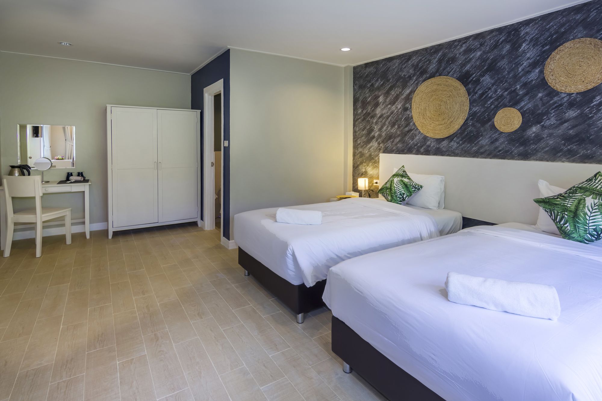 A hotel room with two beds, a desk with a chair, and a wardrobe.