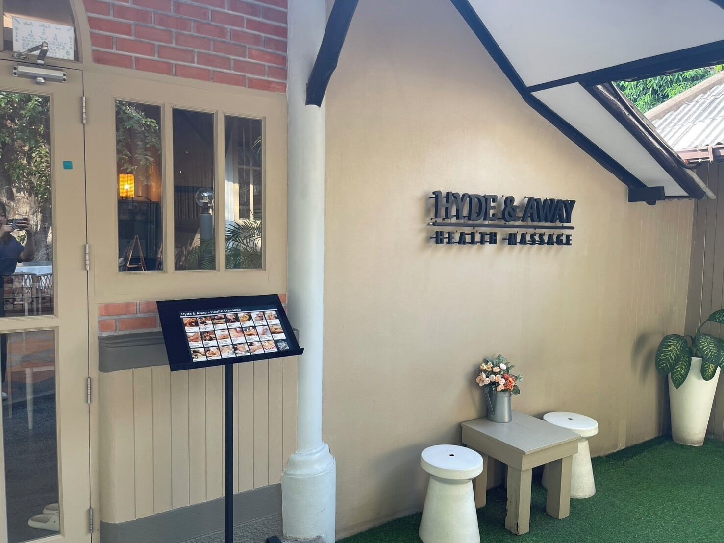 Um centro de massagem para saúde chamado 'Hyde & Away', com uma placa, um mural de imagens e dois banquinhos com plantas em vasos.