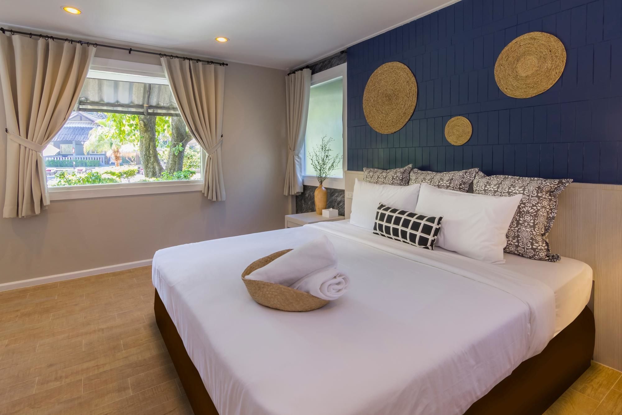 A neatly made bed with a rolled towel, a nightstand with a vase, and a window with curtains.