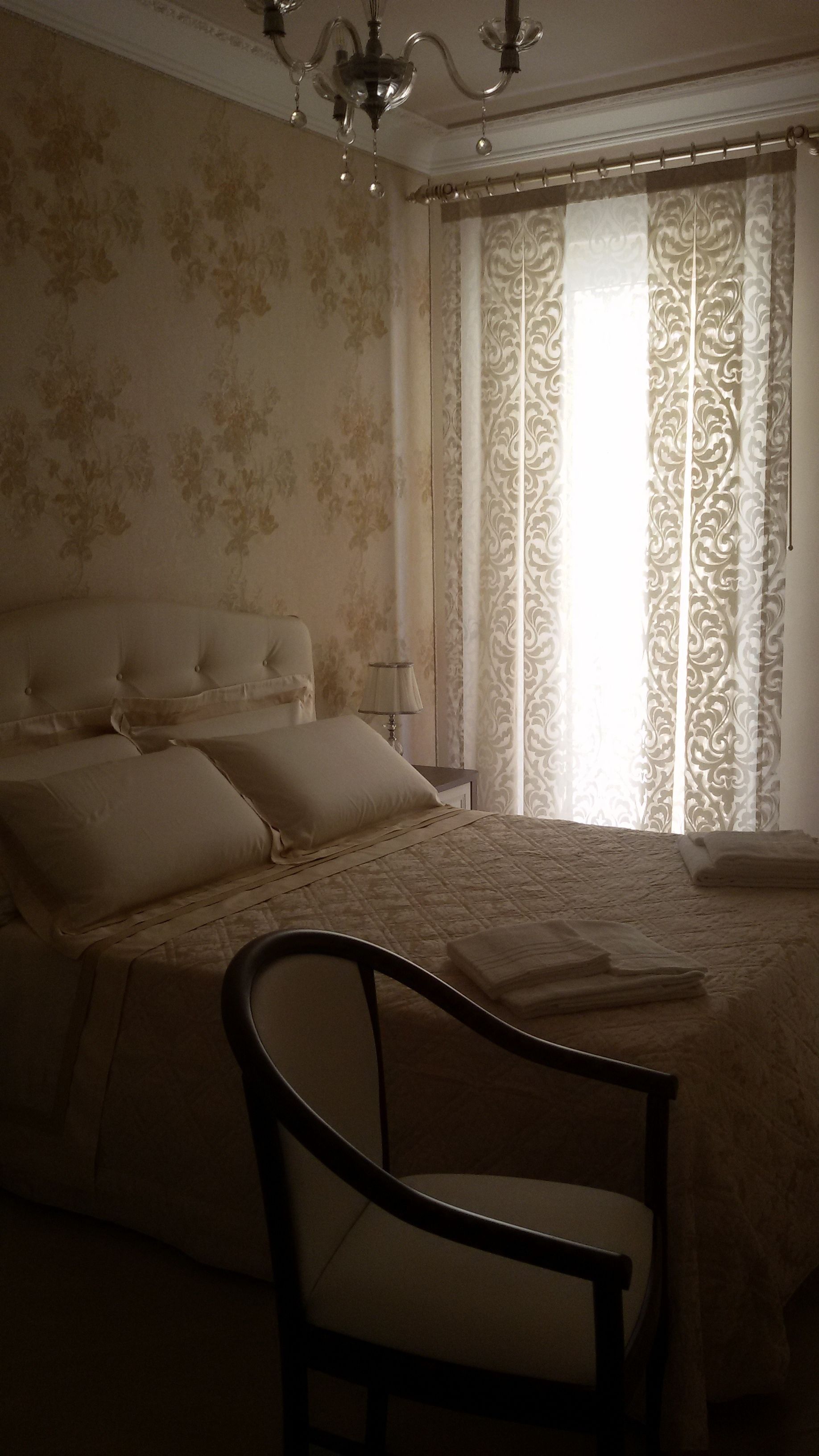 A bedroom with a large bed, a chair, a nightstand, and a chandelier.