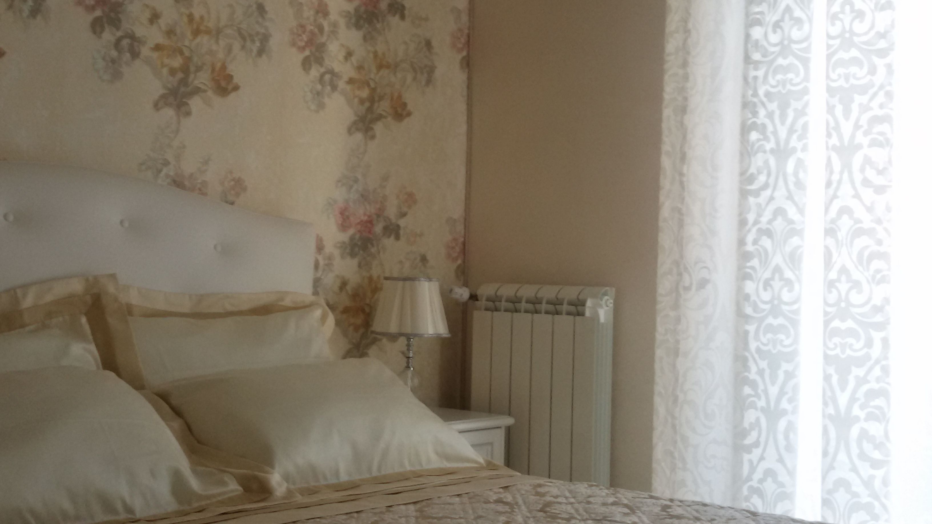 Un dormitorio con cama, mesita de noche, lámpara y radiador.