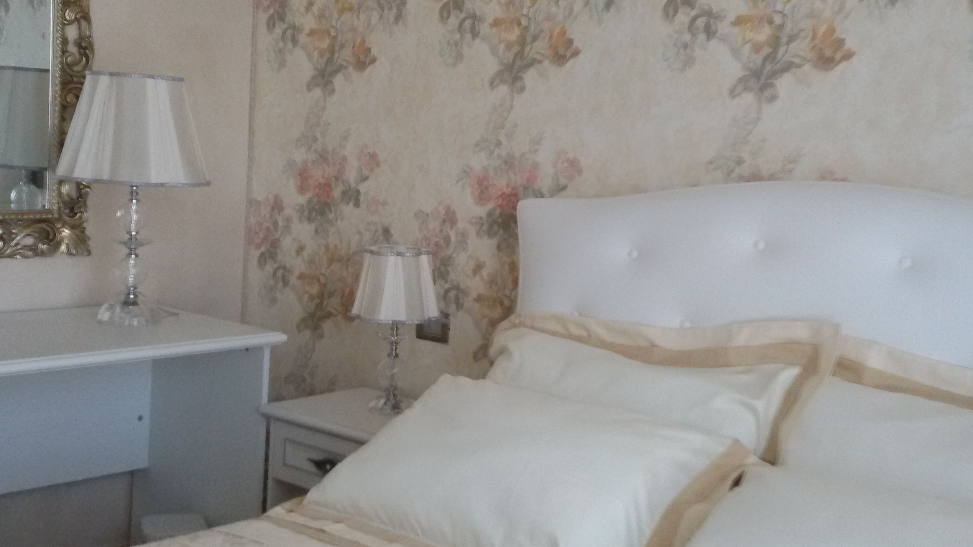 Ein Schlafzimmer mit einem Bett, zwei Nachttischen, einem Spiegel und blumigem Wandpapier.