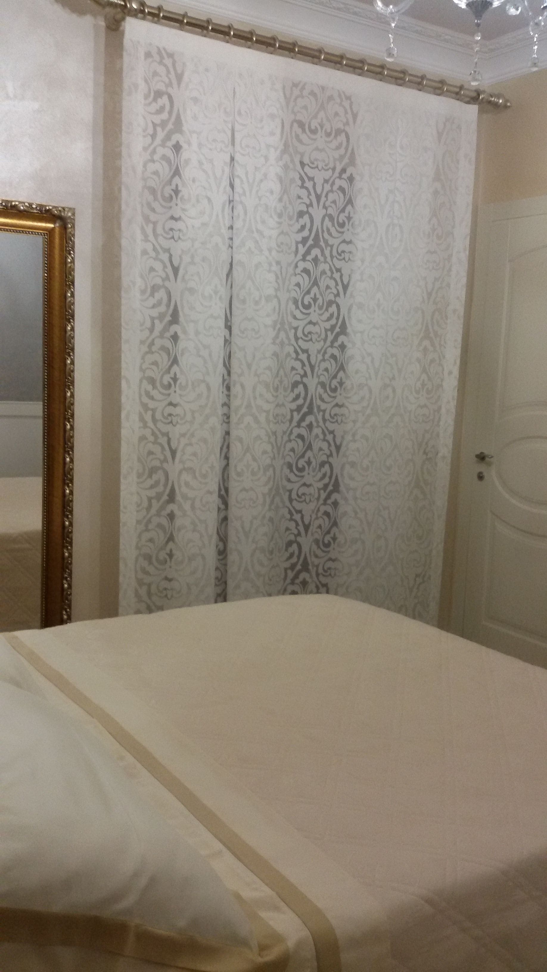 A bedroom with a bed, a mirror, a door, and a curtain with a floral pattern.