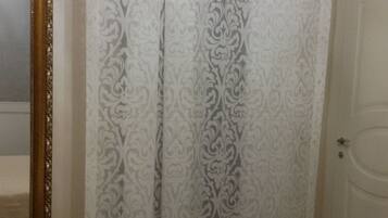 A bedroom with a bed, a mirror, a door, and a curtain with a floral pattern.